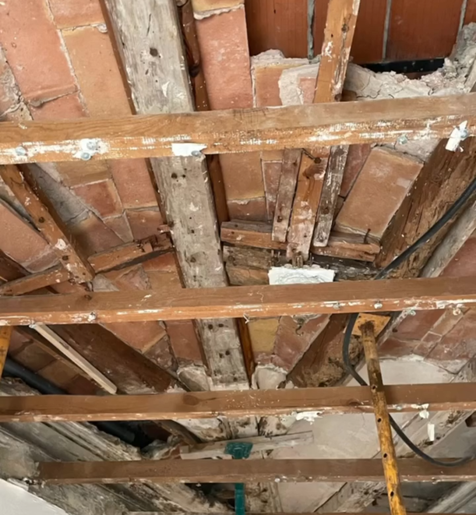 Exposed ceiling structure with damaged wooden beams and bricks, showing signs of deterioration; construction scaffolding visible below. Label "ANTES" at the bottom.