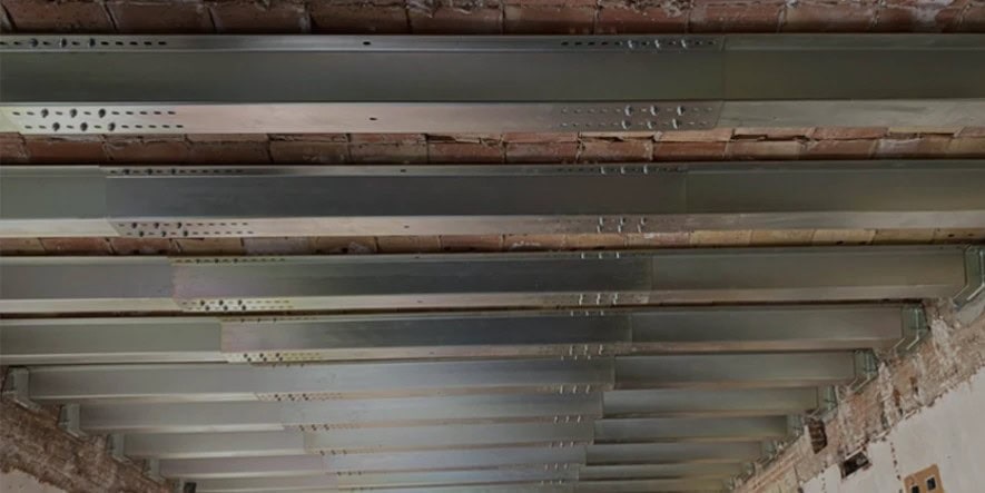 Exposed steel beams with metal plates are installed across a ceiling in a building under construction or renovation.